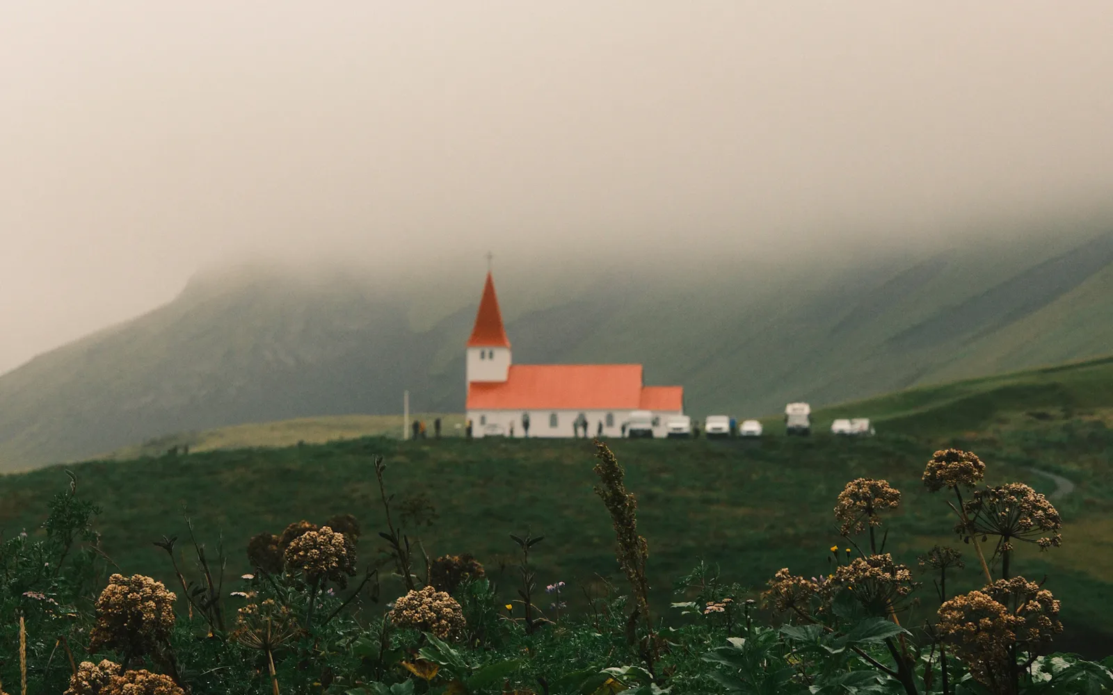 Red-roofed Vík church beneath rolling hills and low cloud; a landscape reference, not a live weather or road report