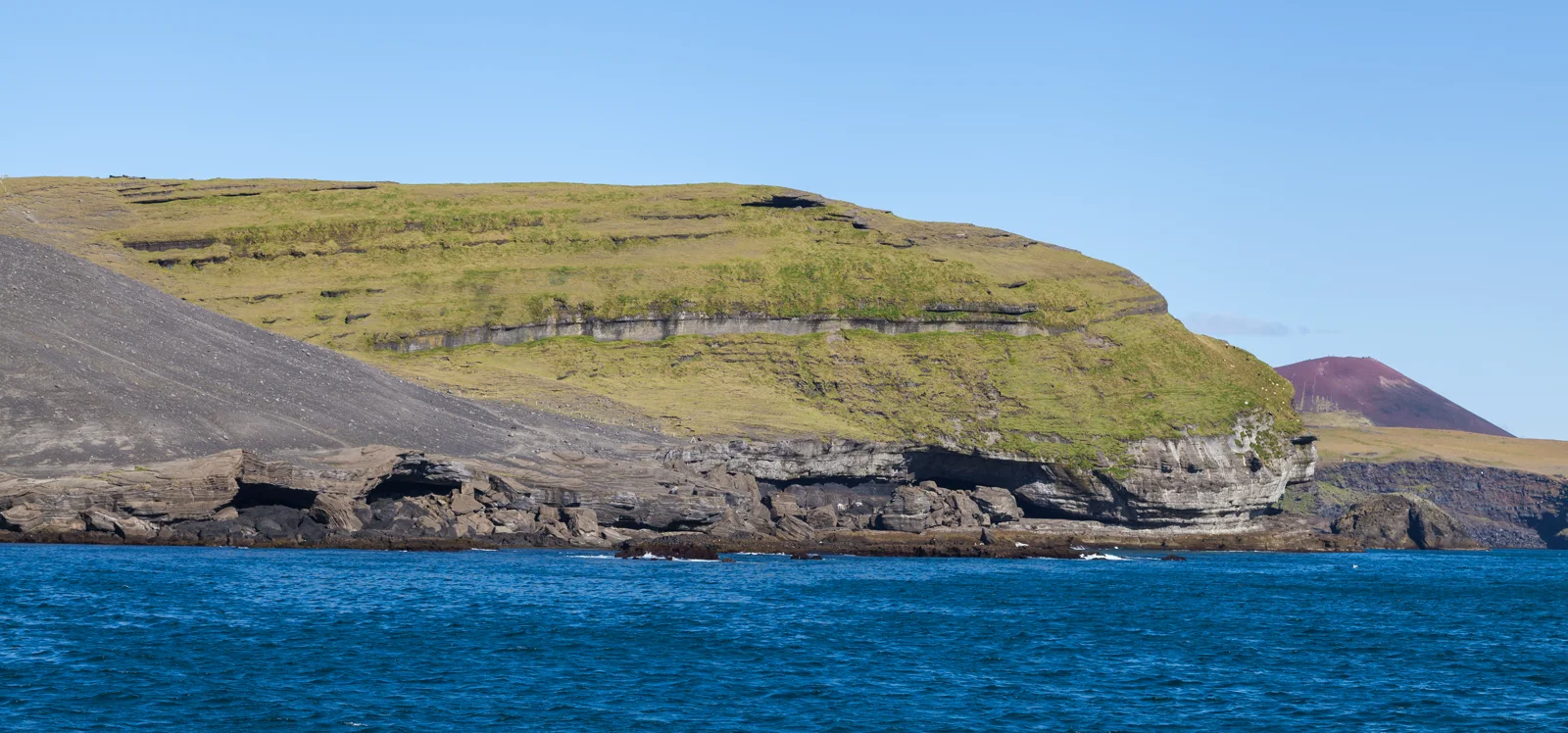 Heimaey volcanic coastline, black rock shore connected to volcanic landscape