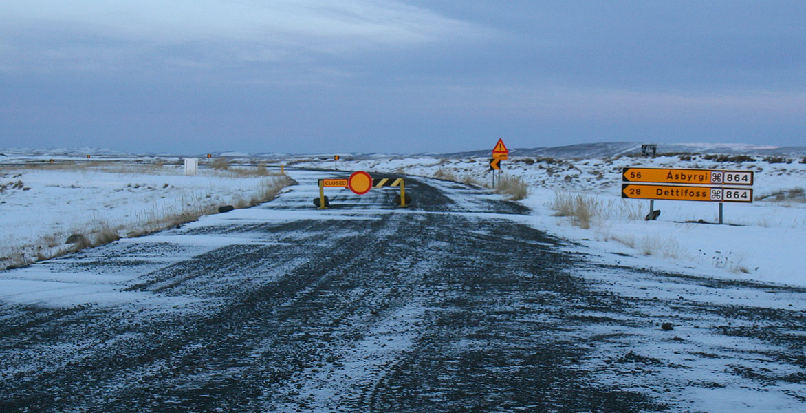 A snow barrier closes the road to Dettifoss beside a Route 864 sign in Iceland; the photograph shows the setting of a closure sign and does not represent current road conditions