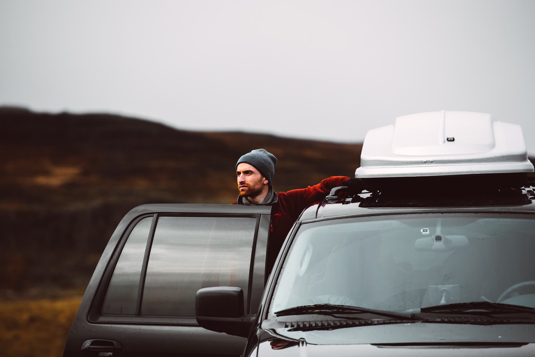 Travellers beside a vehicle organising a roof box during an Iceland trip, illustrating the practical work created by luggage and vehicle height