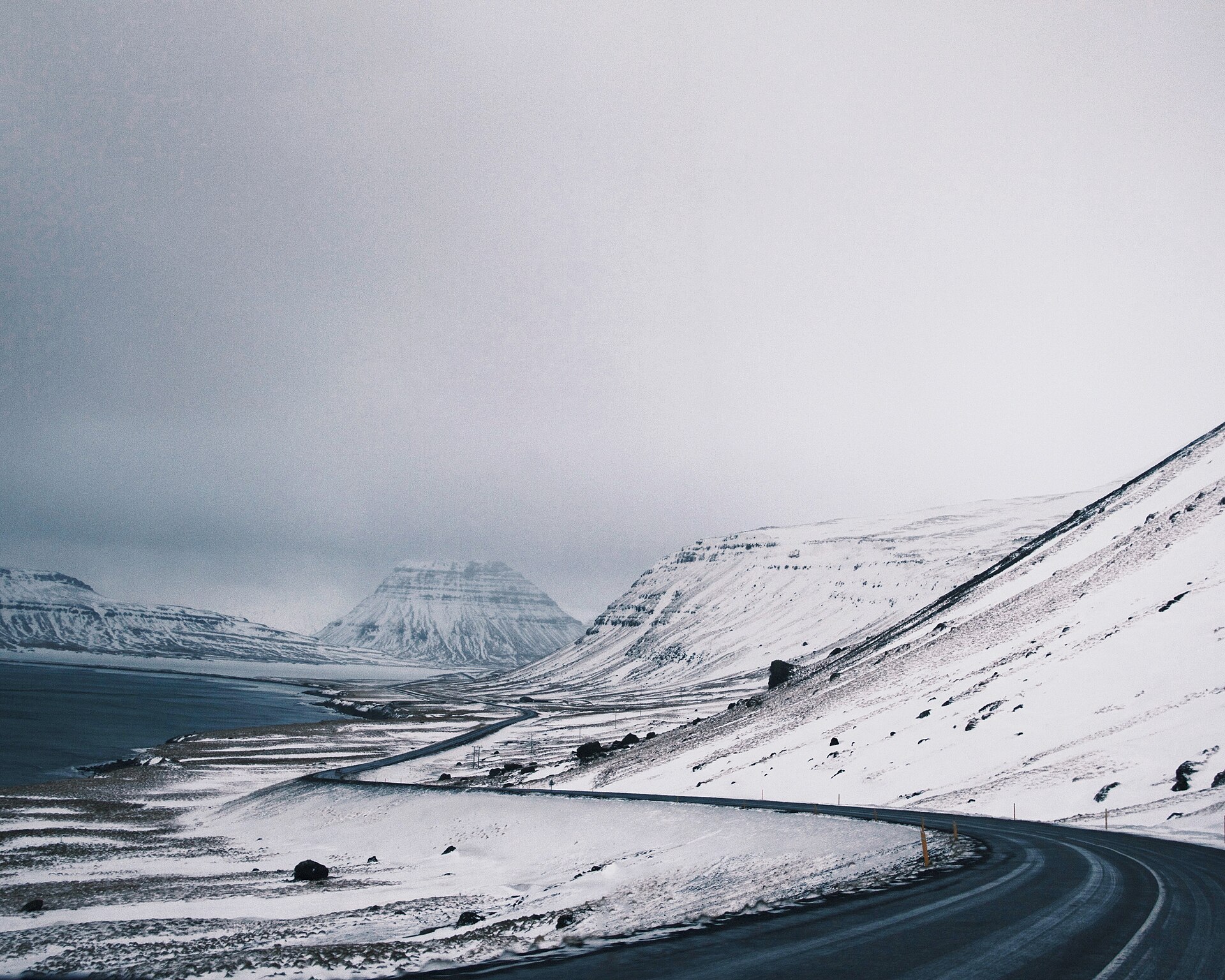 Snowy Iceland coastal road bend with roadside markers and low cloud