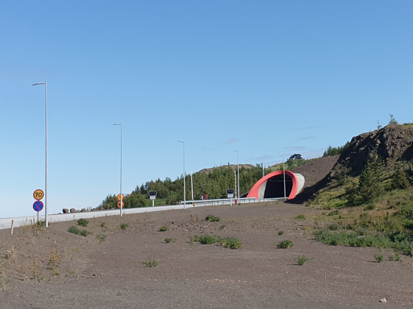 A real photograph of the Vaðlaheiðargöng tunnel entrance and a 70 km/h speed-limit sign; it does not represent today's toll or road conditions