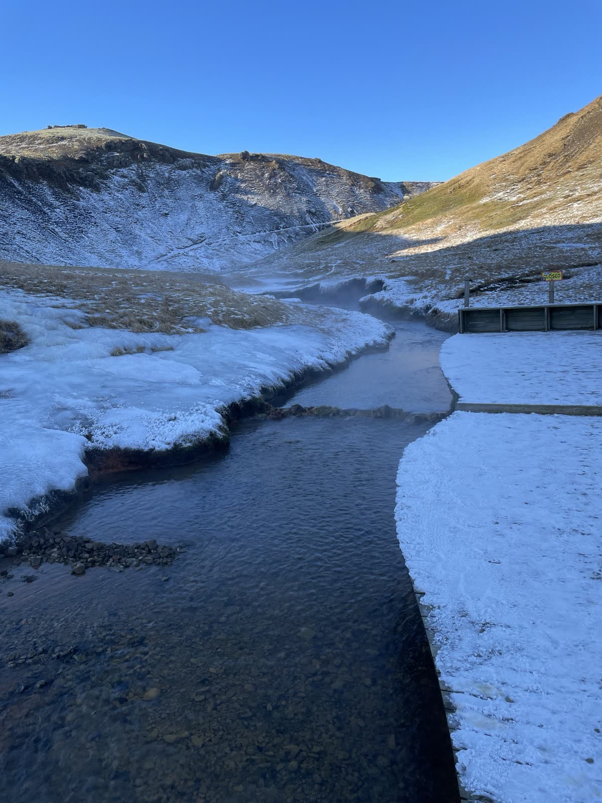 Reykjadalur hot river in winter, with snow and a CLOSED sign beside the path