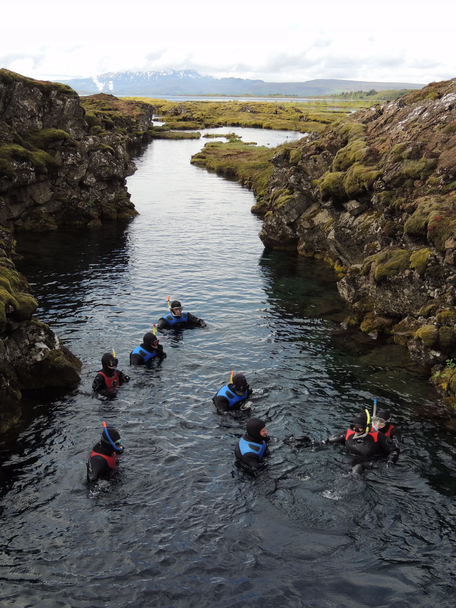 A guide and dry-suited snorkeller in Silfra, between moss-covered rock walls