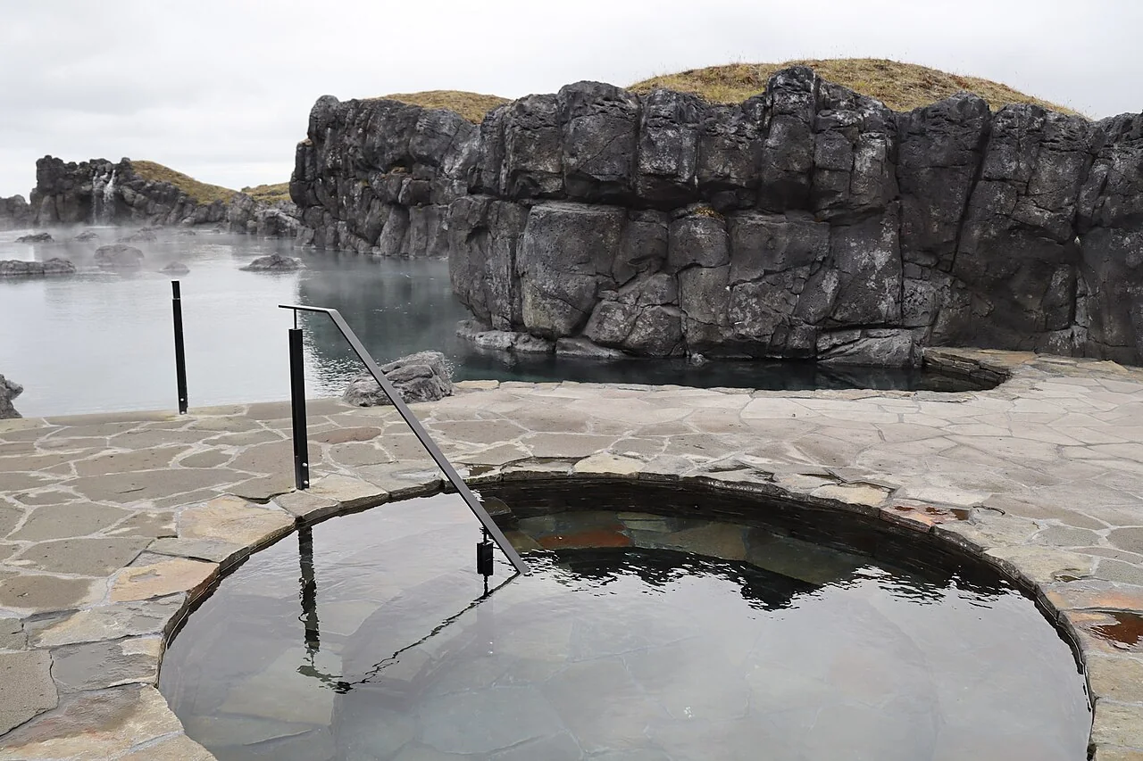 Real Sky Lagoon venue, with a cold plunge in front and the geothermal pool backed by dark rock walls