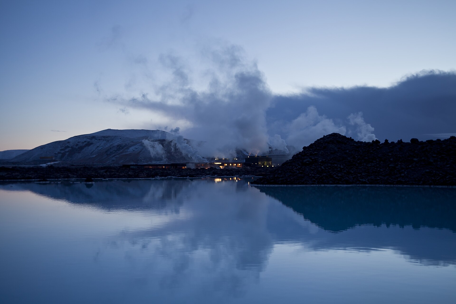 The Blue Lagoon at dusk, with milky-blue water, steam, lava and low buildings