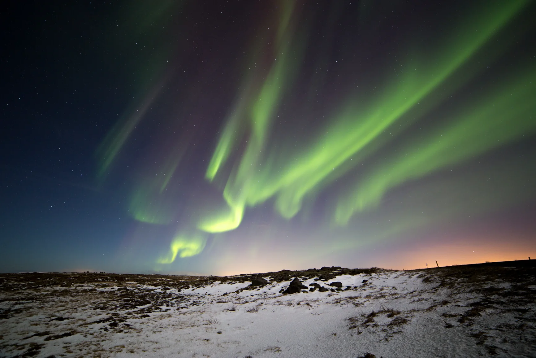Green aurora above snowy ground and lava rocks in Iceland