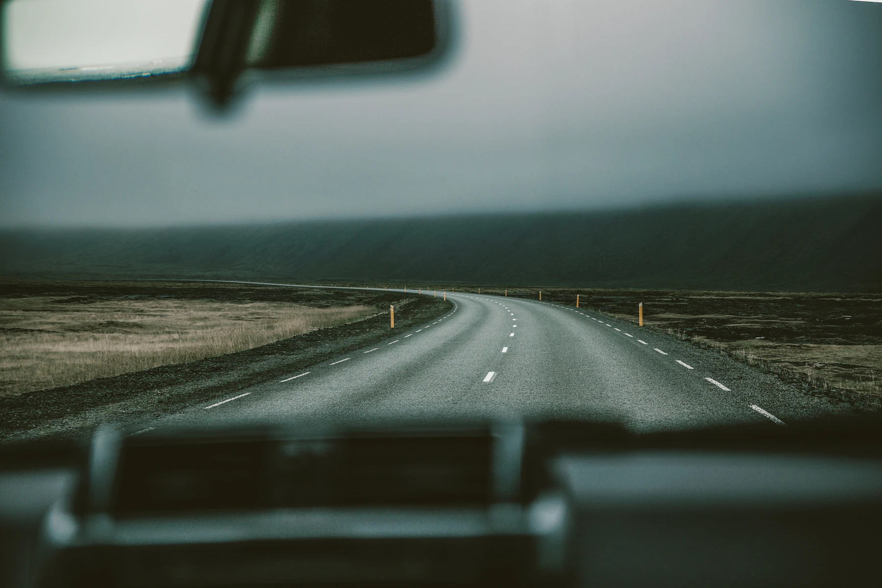 View from inside a car looking out onto an Icelandic paved road, road signs, and distant mountain scenery